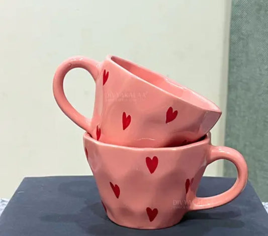 Two pink mugs with red heart patterns stacked on a dark surface.