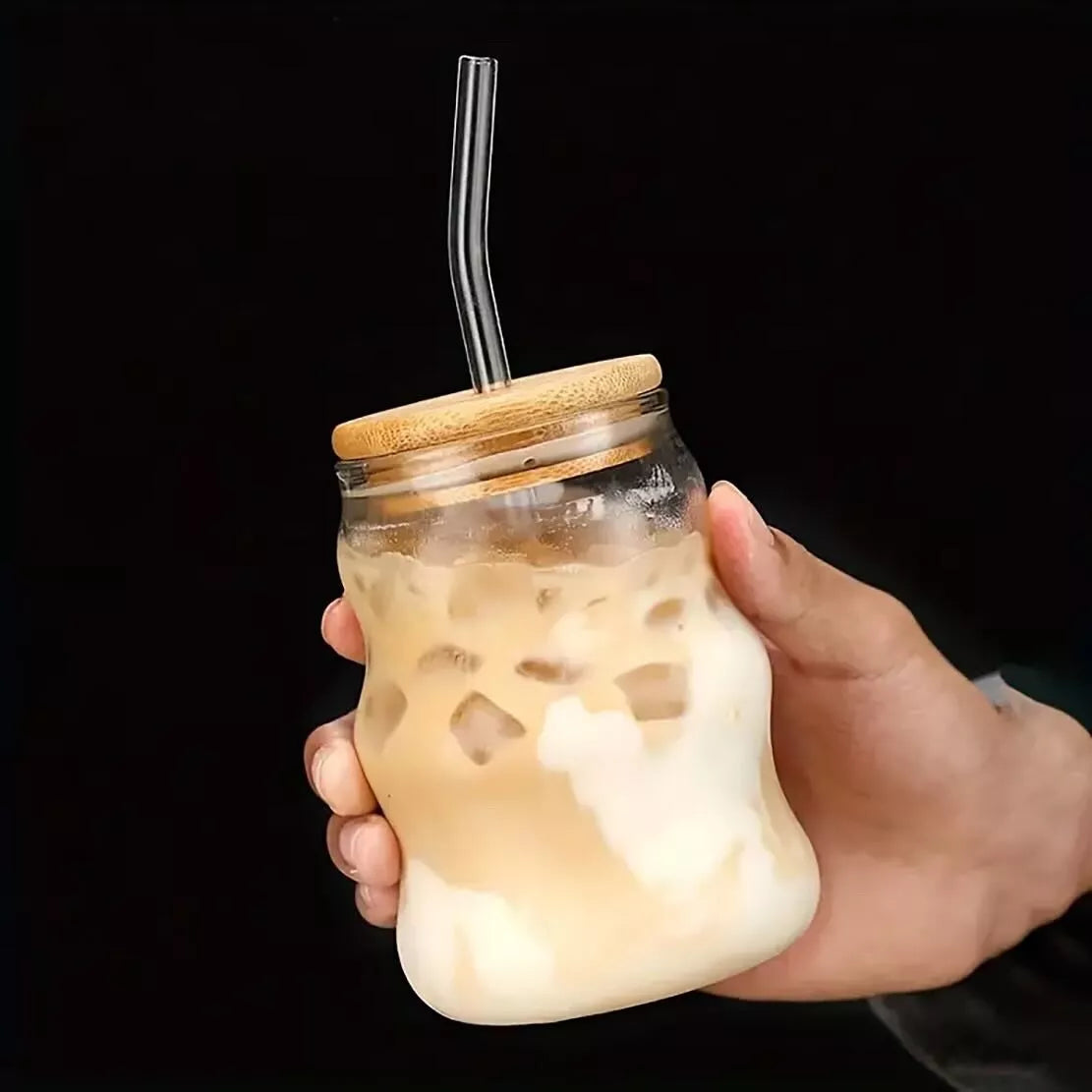 Hand holding a glass jar with iced coffee and a straw, against a black background